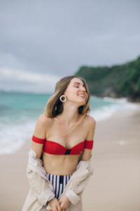 Young woman standing at beach against sky