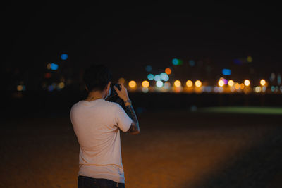 Rear view of man standing on illuminated city at night