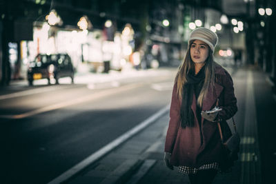 Mid adult woman looking away while standing on city street at night