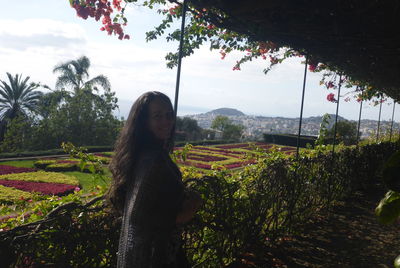 Portrait of woman standing by plants against sky