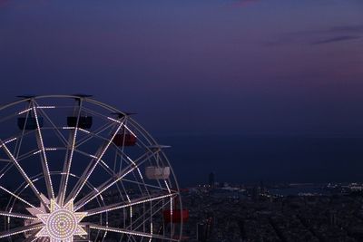 Ferris wheel by illuminated buildings against sky at night