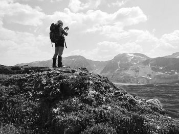 Hiker with backpack photographing on mountain against sky