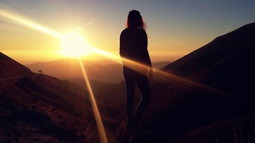 Rear view of silhouette woman standing against mountains during sunset