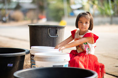 Girl sitting by bucket outdoors