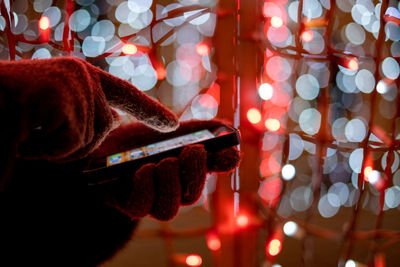 Cropped hands using phone against illuminated christmas lights