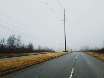 Road by electricity pylons against clear sky