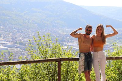 Portrait of couple flexing muscles while standing at observation point against mountain