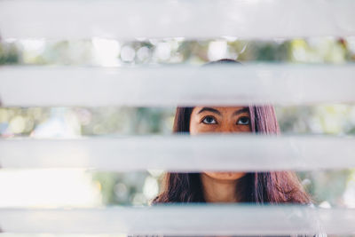 Woman looking away seen through blinds against window
