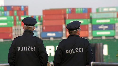 Rear view of police men standing by railing against containers