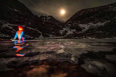 Reflection of person in lake against mountain at night