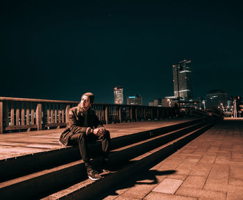 Young man sitting on retaining wall at night