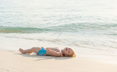 Blond haired todler laying in the sand at the beach
