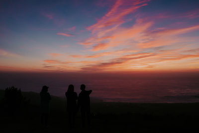 Silhouette people standing on land against sky during sunset