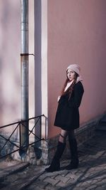 Full length of woman standing on cobbled street by pink wall