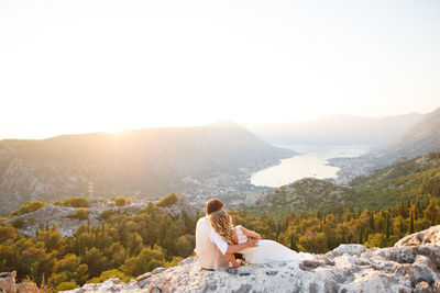 Woman sitting on mountain against clear sky