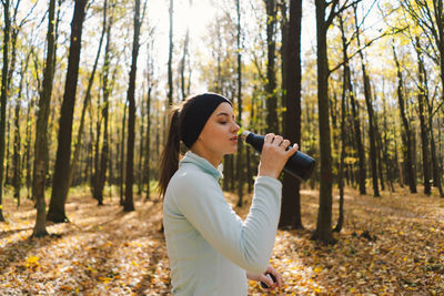 The girl drinks water. a beautiful girl is doing fitness outdoors in a sunny autumn forest