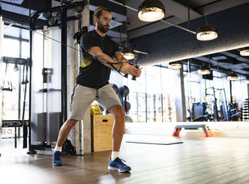 Side view of strong male lifting heavy weights on exercise machine while standing in lunge posture