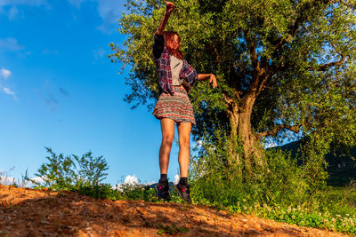 Woman standing by tree against blue sky