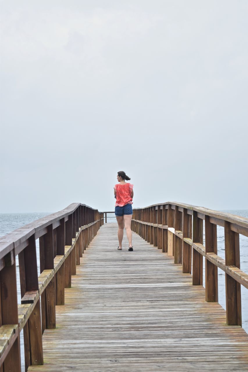 REAR VIEW OF PERSON WALKING ON PIER