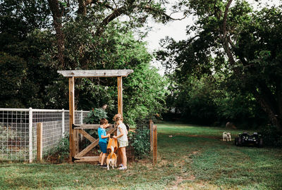 Two young kids opening gate to back yard garden with corgi