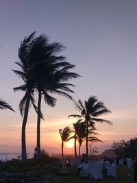 Silhouette palm trees by swimming pool against sky during sunset