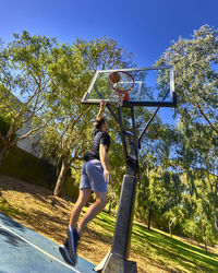 Man putting ball in basketball hoop against clear sky