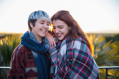 Cheerful lesbian couple standing against clear sky during sunset