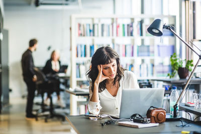 Worried female entrepreneur looking at laptop while sitting in office