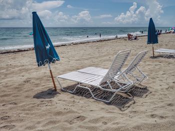 Deck chairs on beach against sky