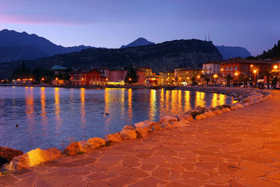 Illuminated city at waterfront during sunset