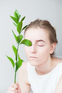 Close-up of young woman with eyes closed holding plant against wall