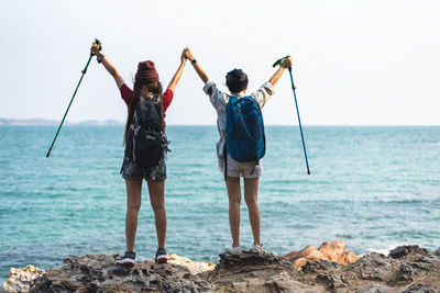 Rear view of friends standing on rock in sea