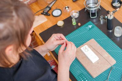 Female jeweler making handmade jewelry at her home studio using a blowtorch and other tools.