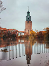 Lighthouse by lake and buildings against sky