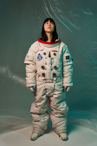 Serious young asian woman in spacesuit with dark hair looking up while standing against green background
