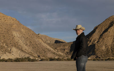 Adult man in cowboy hat standing against mountains in tabernas desert. almeria, spain