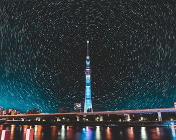 Illuminated tower against star trails in city at night