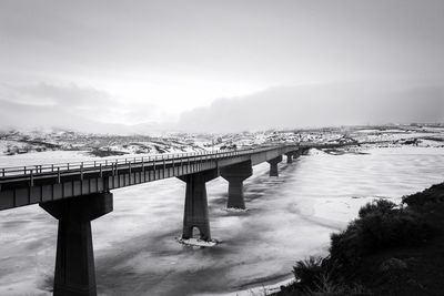 Bridge over frozen river against sky