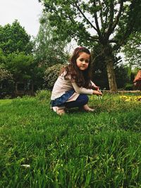 Side view portrait of girl crouching on grassy field