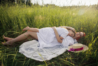 Girl a child hug mother mother with red hair lying on a green field at sunset