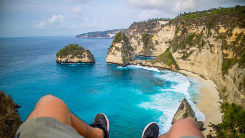 Low section of people on rock by sea against sky