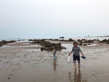 Rear view of men walking on beach against sky