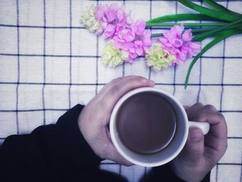 Directly above shot of hands holding coffee cup by flowers on table