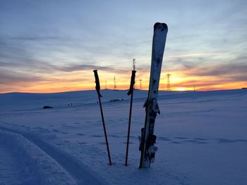 Skis and ski poles in the snow with sunset in the background