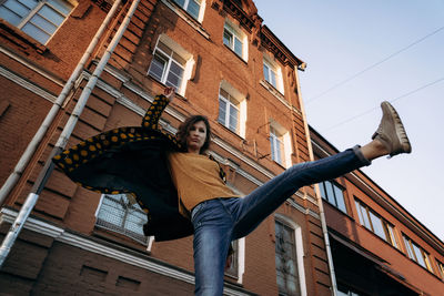 Low angle portrait of young woman standing against building in city