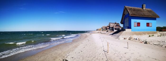 Scenic view of beach by building against blue sky