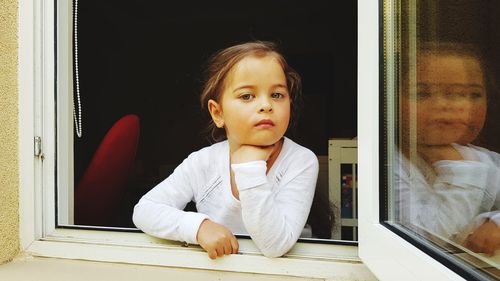 Portrait of cute girl looking through window at home