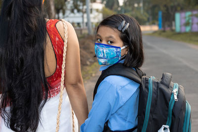 An indian school girl child going to school again after pandemic wearing nose mask protection