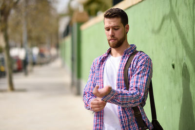 Man buttoning shirt sleeve while standing against wall