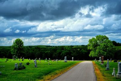 Road passing through field against cloudy sky